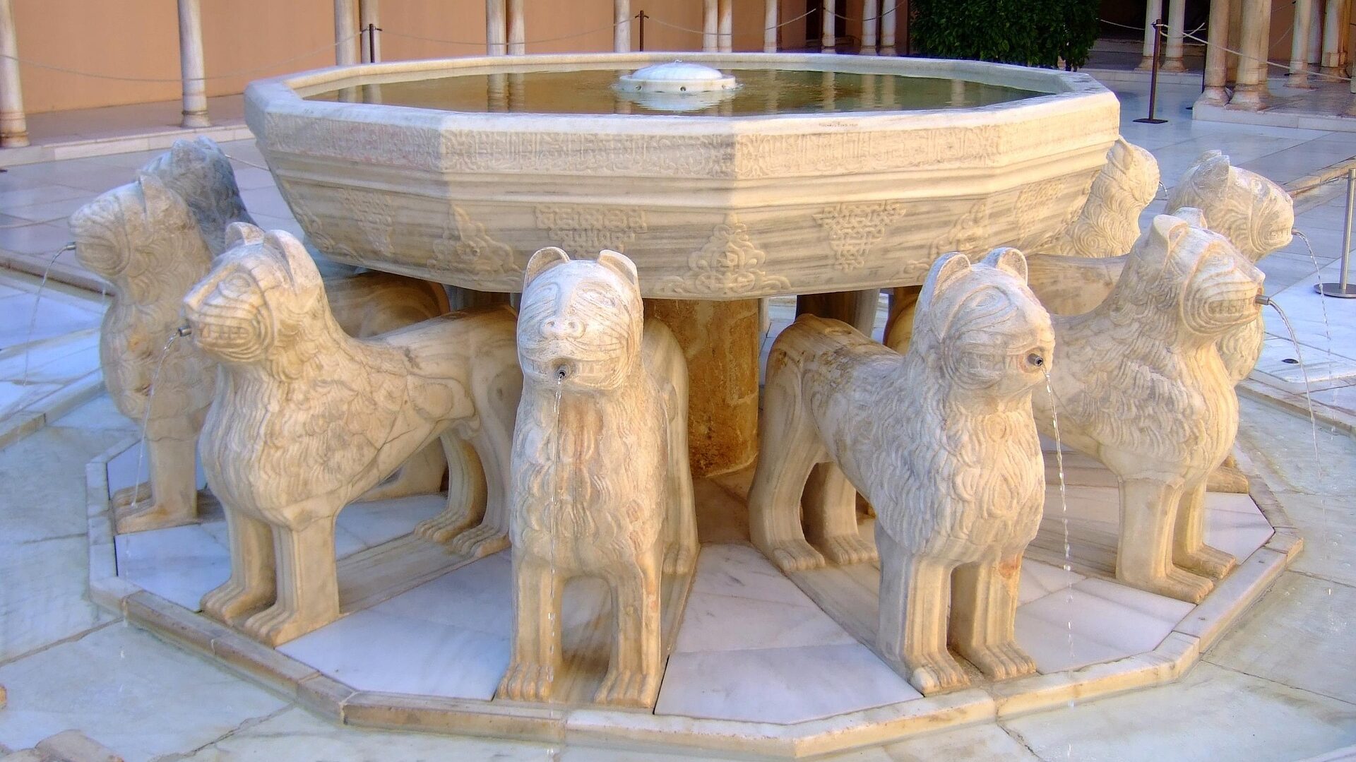 Detalle de la fuente de los doce leones de mármol en el Patio de los Leones de la Alhambra, con agua fluyendo de las bocas de las esculturas sobre un pavimento de mármol blanco.